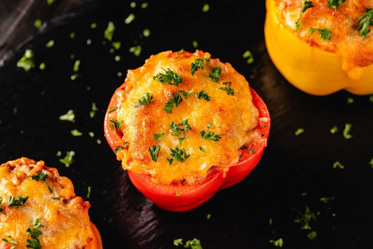 Three grilled stuffed peppers on a black platter sprinkled with parsley.