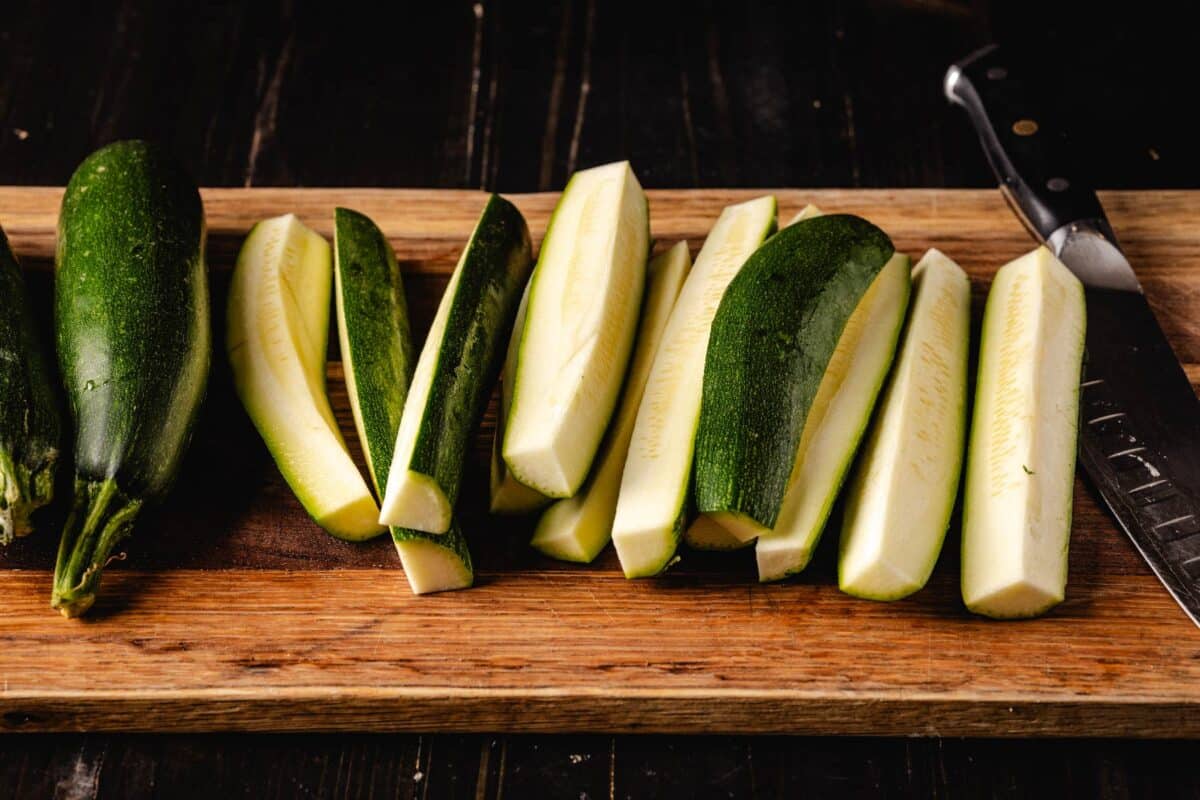 Sliced squash spears on a wooden cutting board with a knife.