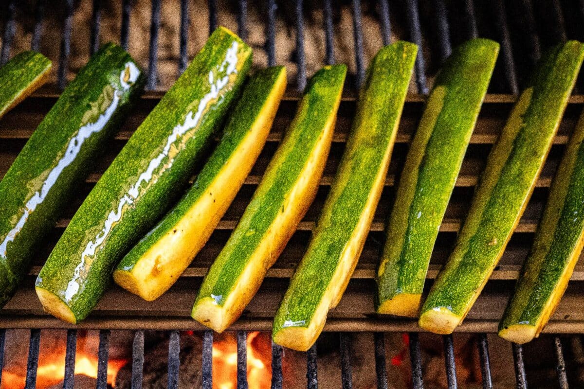 Marinated zucchini spears on grill grates.