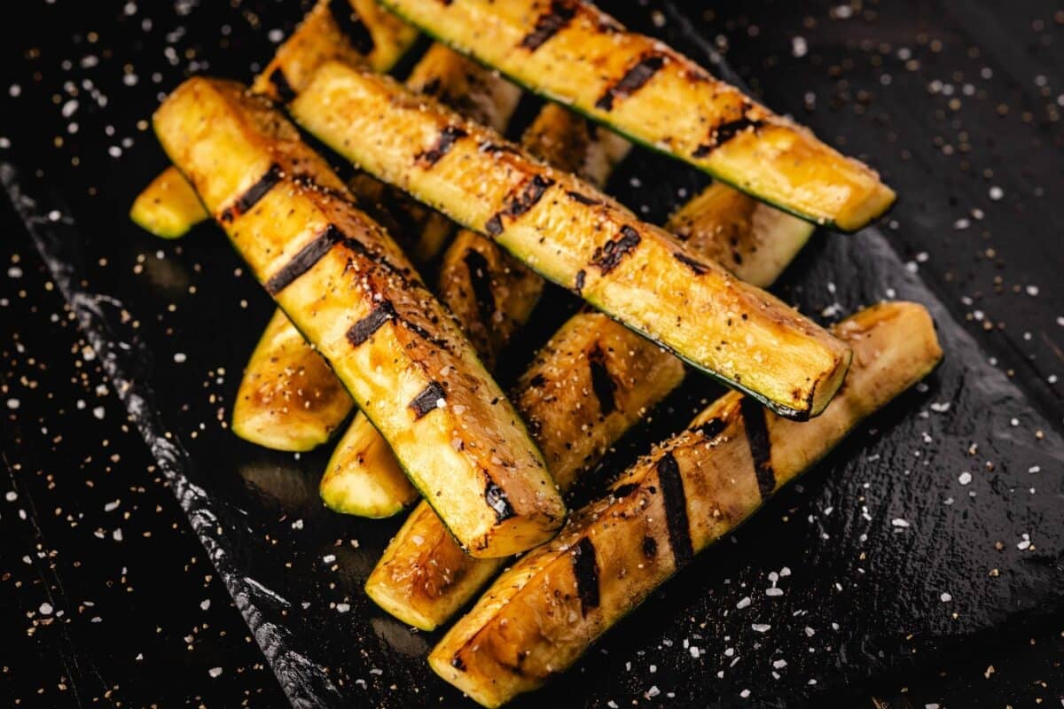 Squash spears with grate marks, piled on a black serving platter, sprinkled with seasoning salt.