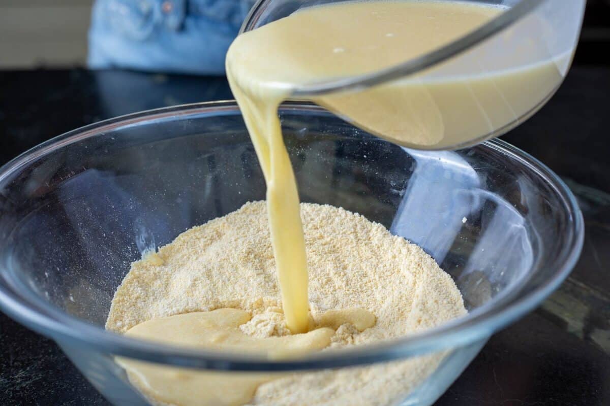 A wet ingredient mix in a glass bowl being poured into a glass bowl with dry ingredients.