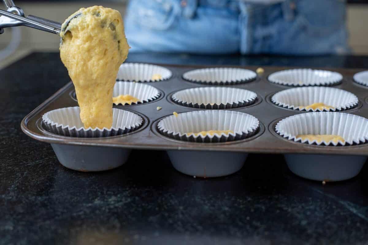 A scoop spooning batter into a muffin tin lined with cupcake liners.