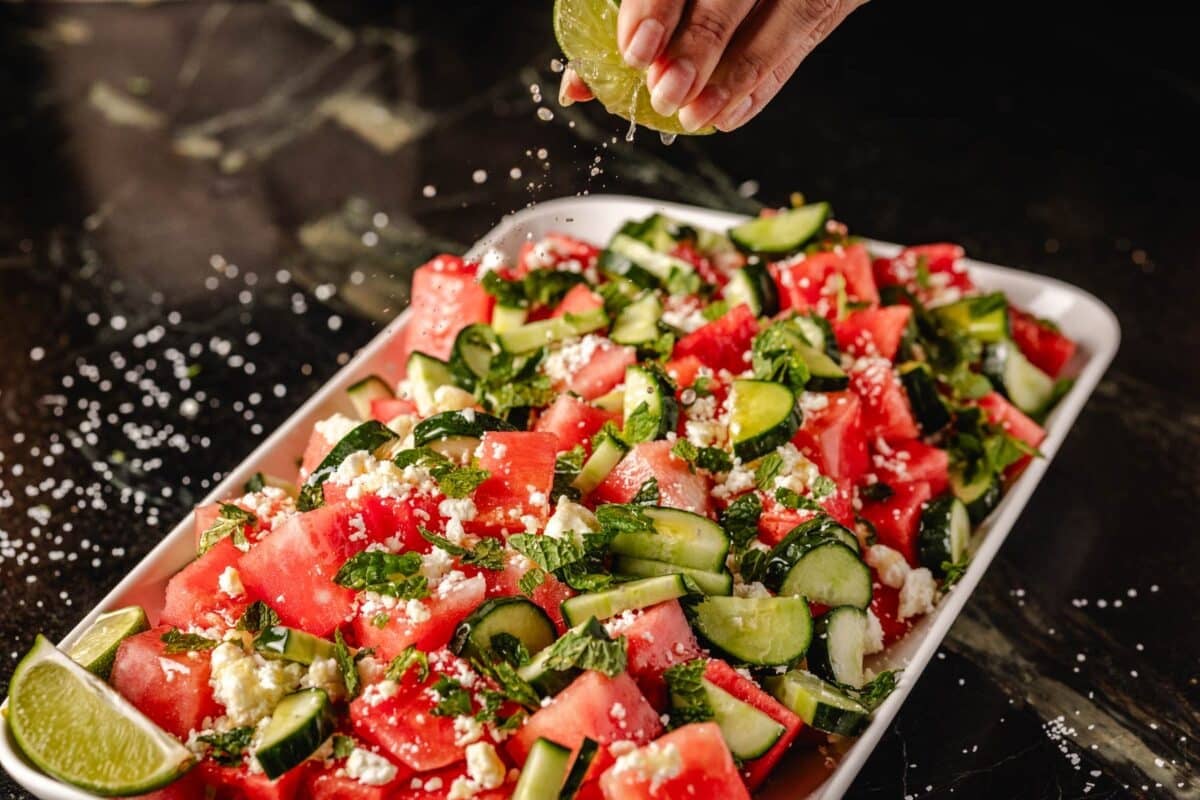 Fruit salad on a serving platter, with a lime being squeezed onto it for juice.