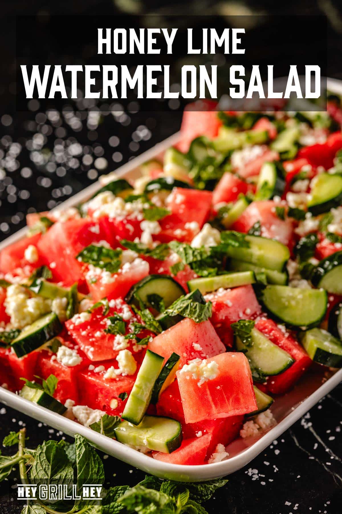 A salad with watermelon, cucumber, and cheese on a serving platter. Text overlay reads "Honey Lime Watermelon Salad."