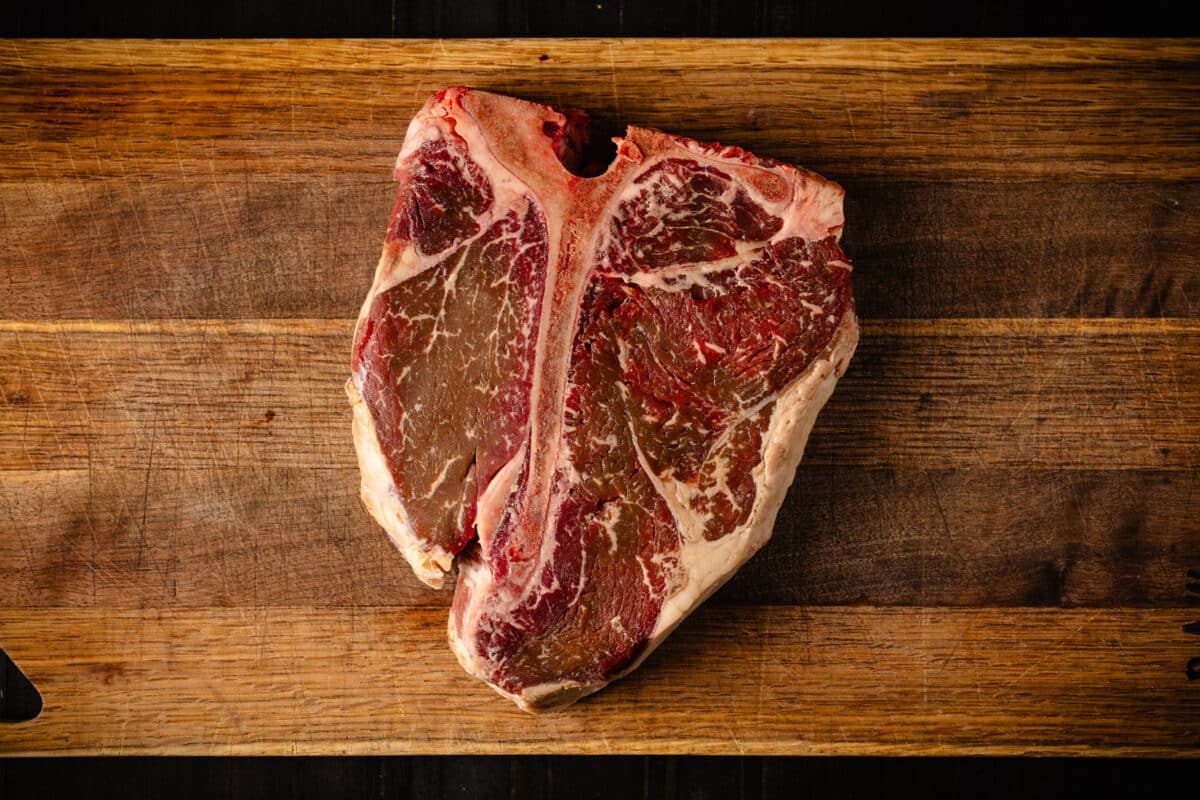 A raw porterhouse sitting atop a wooden cutting board.