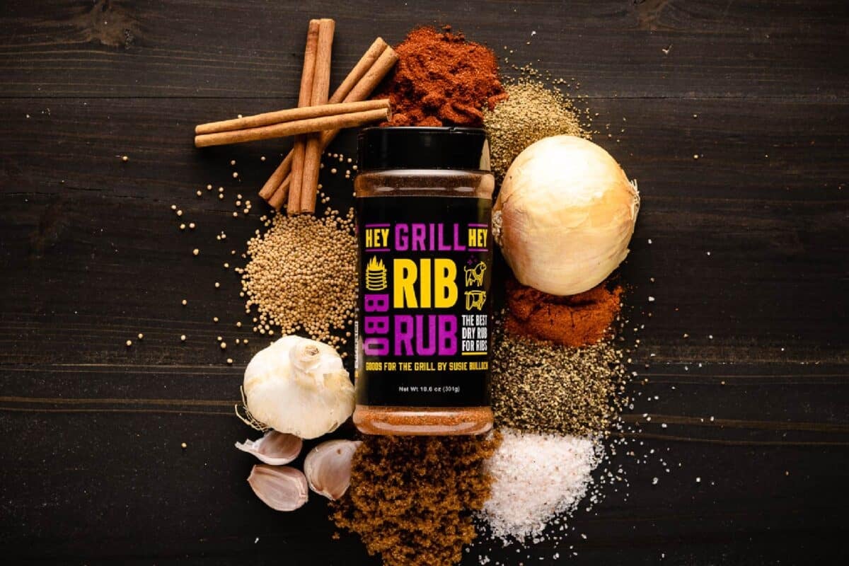 A bottle of Rib Rub on a countertop surrounded by raw ingredients.