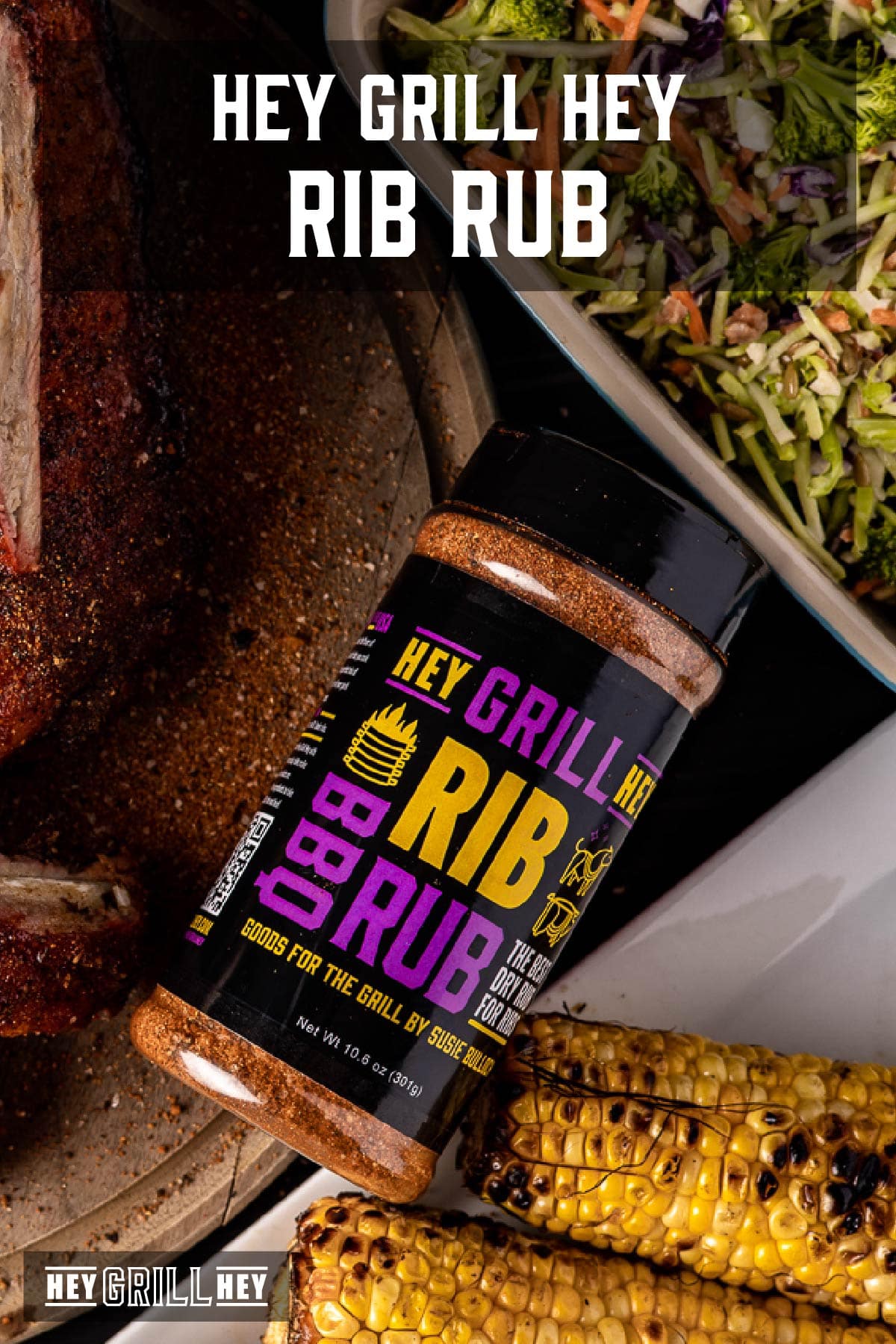 Bottle of Rib Rub next to assorted grilled meats and vegetables on a table. Text overlay reads "Hey Grill Hey Rib Rub."