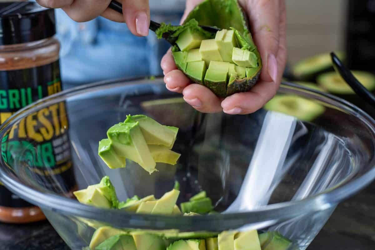 A sliced avocado half being scooped into a glass bowl with a spoon.