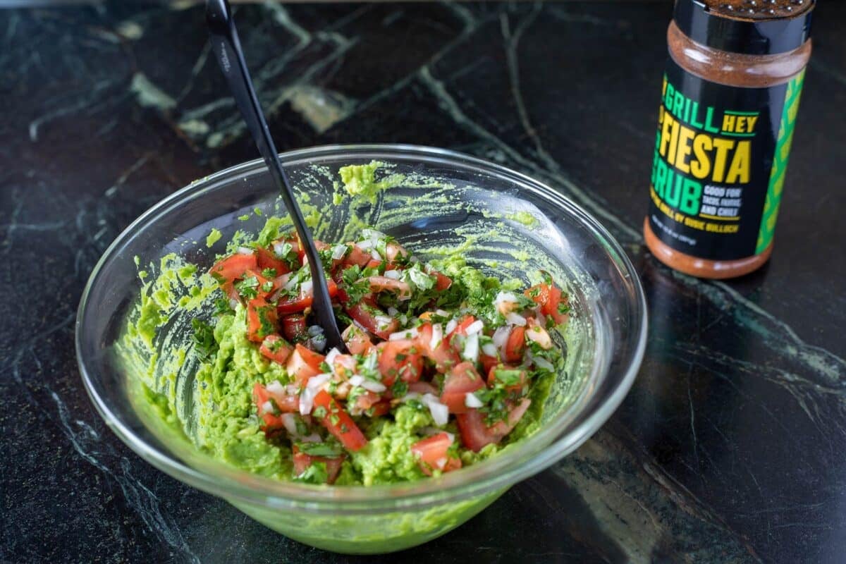 Unmixed guacamole in a glass bowl on a counter next to a bottle of rub.