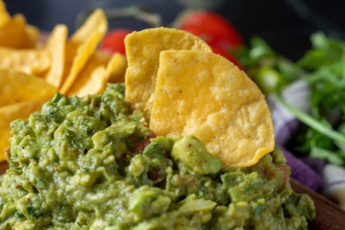 Tortilla chips resting in a bowl of guacamole.