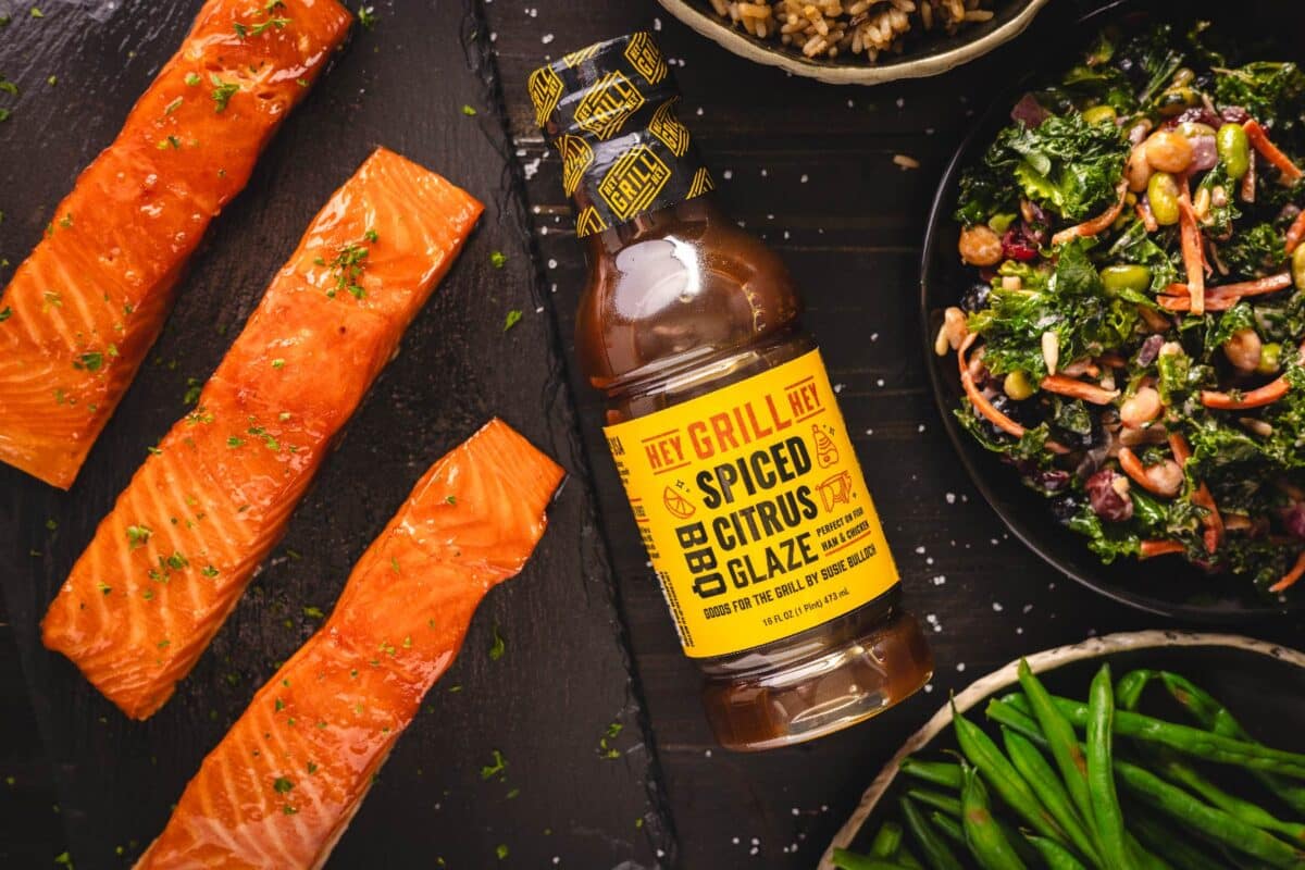 Slices of cooked salmon fillets next to a bottle of sauce, and bowls of side dishes.