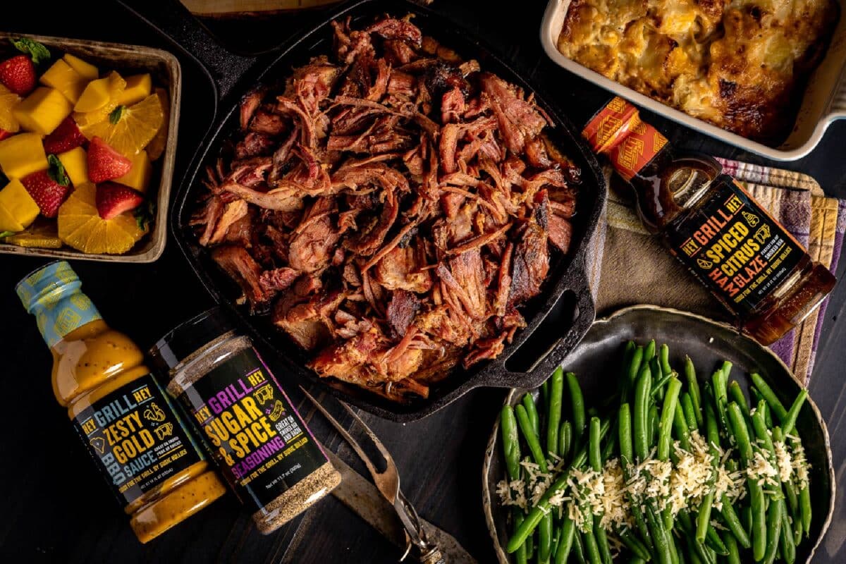 Shredded ham in a skillet on a table with season and sauce jars, and side dishes.