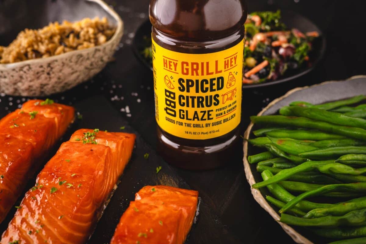 A bottle of Spiced Citrus Glaze next to plates of salmon and green beans.