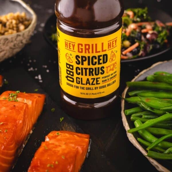 A bottle of Spiced Citrus Glaze next to plates of salmon and green beans.