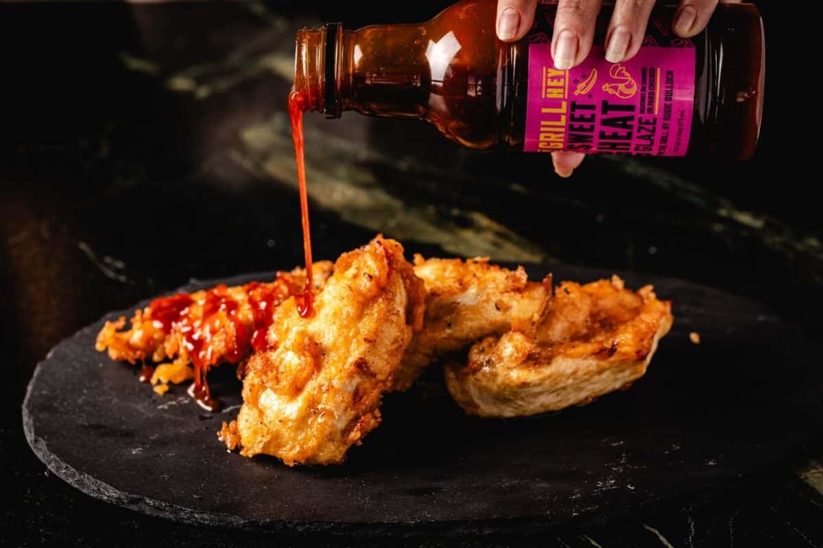 Fried chicken tenders piled on a black stone platter being drizzled with BBQ sauce.