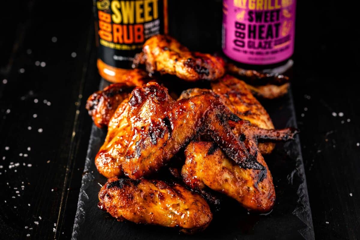 Smoked chicken wings on a black serving platter in front of bottles of BBQ rub and sauce.