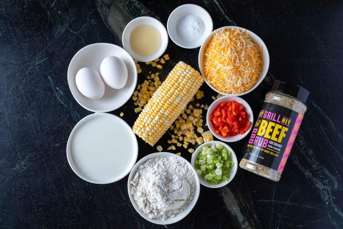 A cob of corn on a table surrounded by bowls filled with peppers, onions, and other ingredients.