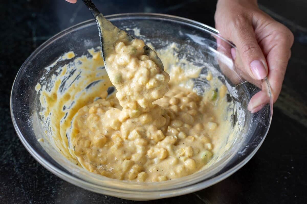 Batter in a clear glass bowl being stirred with a spoon.