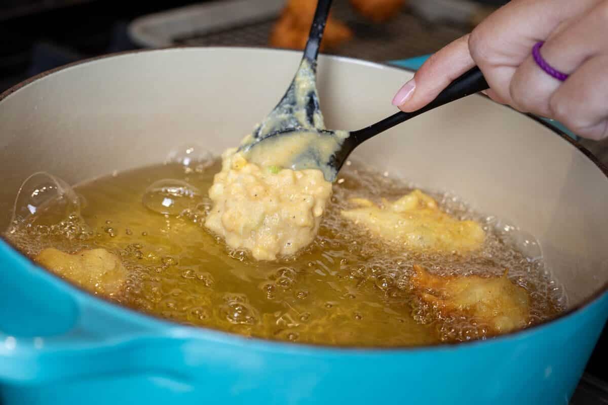 A spoon dropping battering into a blue pot of frying oil.