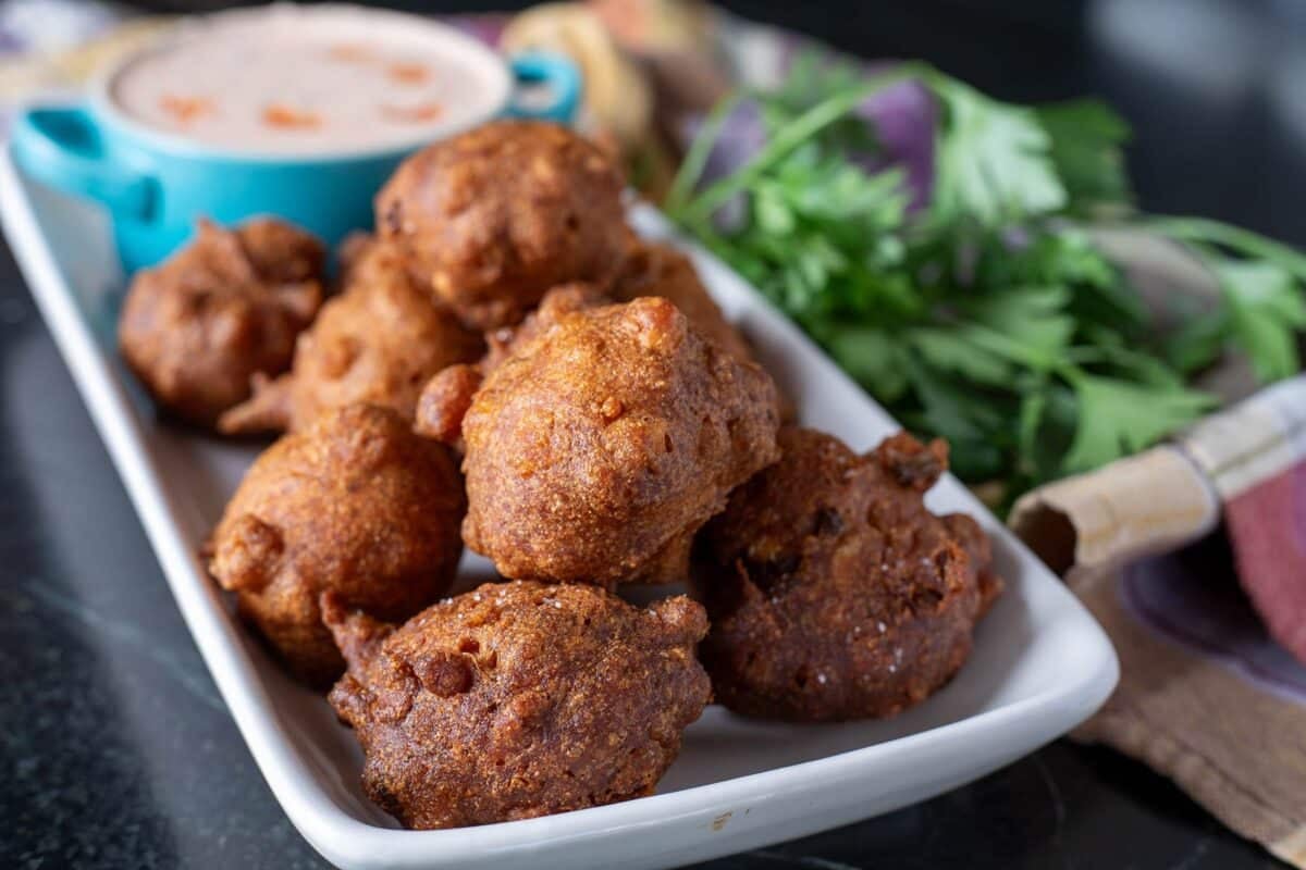 Hush puppies and a blue cup with sauce on a white plate, next to a garnish.