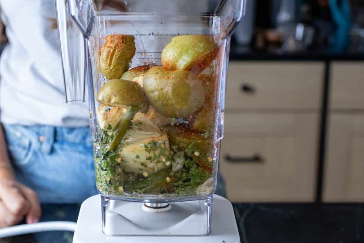 A blender filled with salsa ingredients on a countertop in a kitchen.