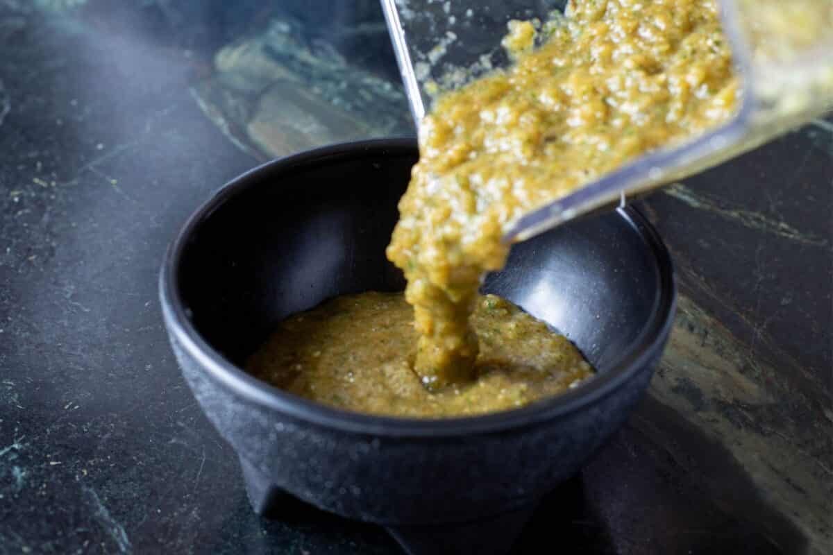 Smoked salsa verde being poured from a blender jar into a black bowl.