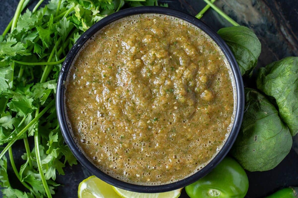 Salsa verde in a black bowl garnished with cilantro leaves and lime wedges.