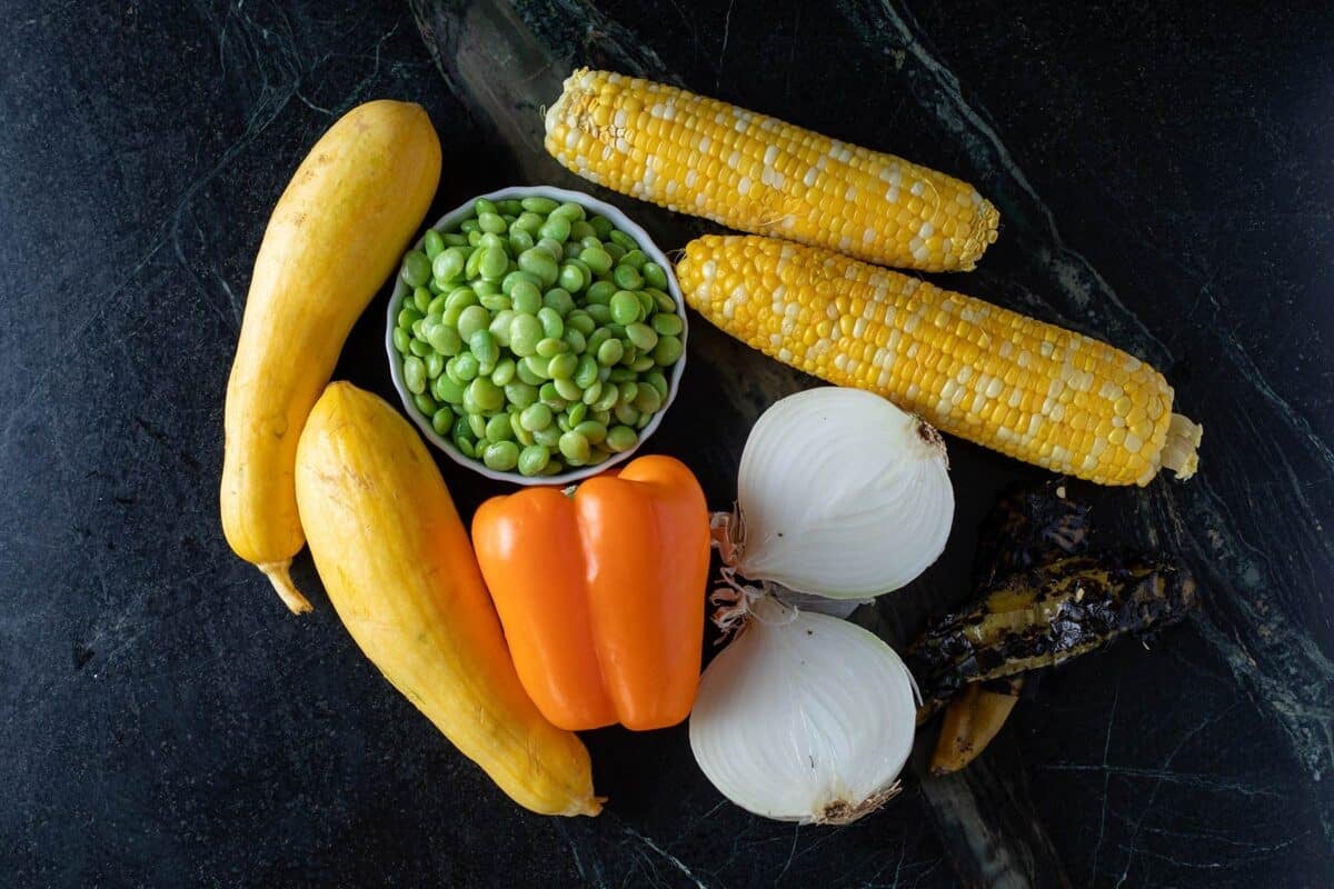 Earns of corn, yellow squash, an orange bell pepper, and other ingredients on a countertop.