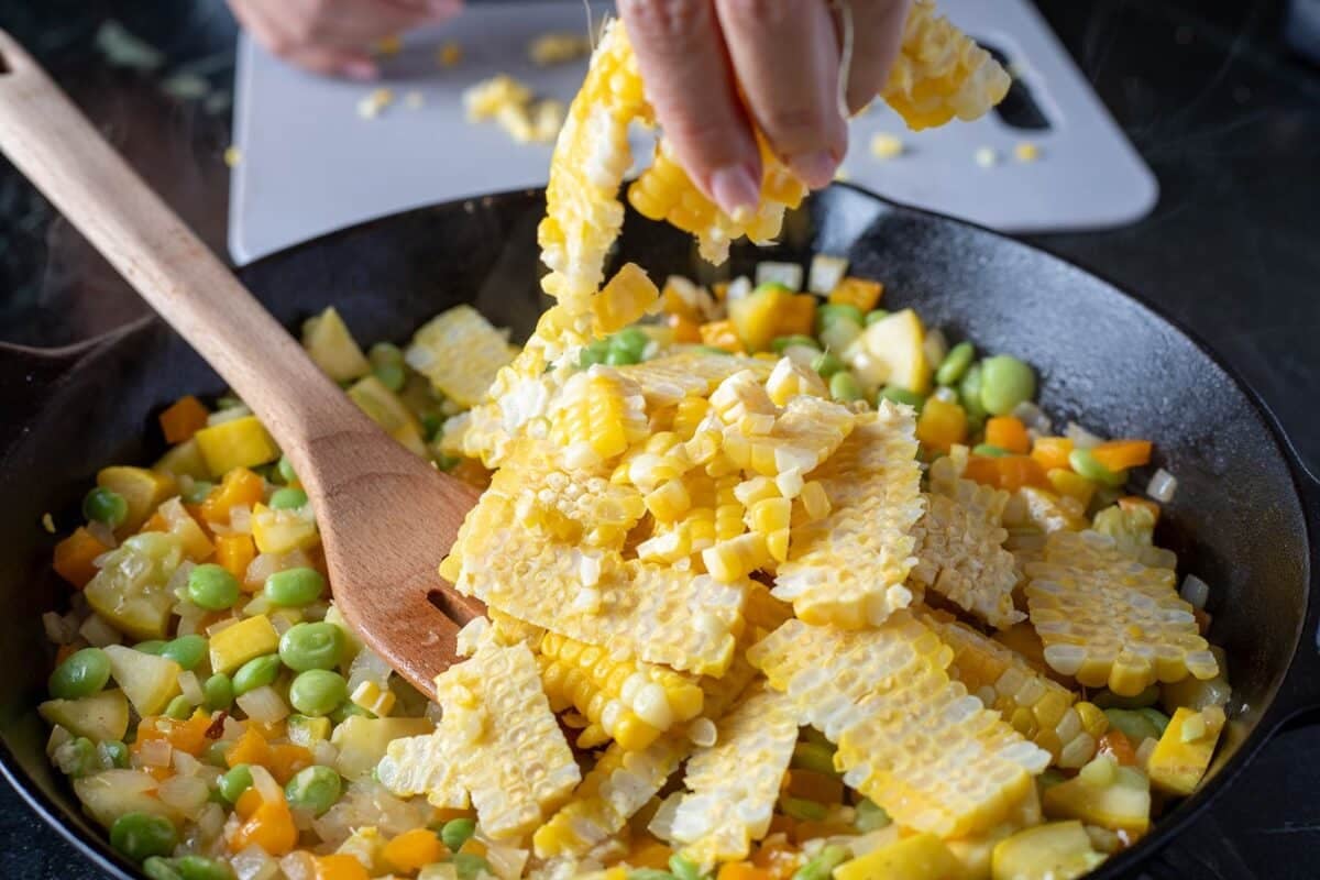 Corn kernels being added to a skillet of chopped veggies.