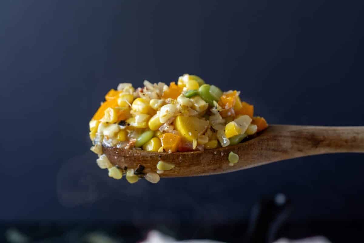 A wooden spoon holding a scoop of succotash.