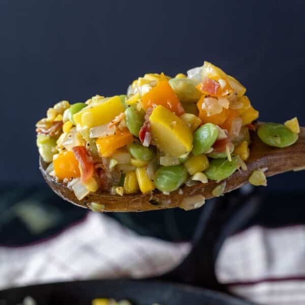 A wooden spoon holding a scoop of succotash.