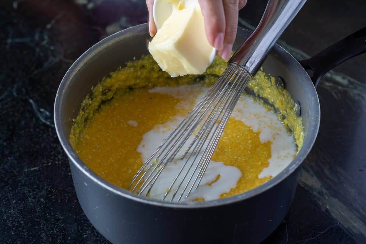 Cream being whisked in a pot, and a cube of butter being added in.