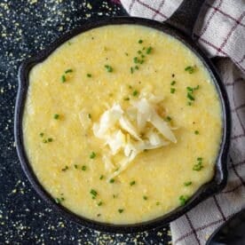 Grits in a cast iron pan topped with chives and shredded cheese.