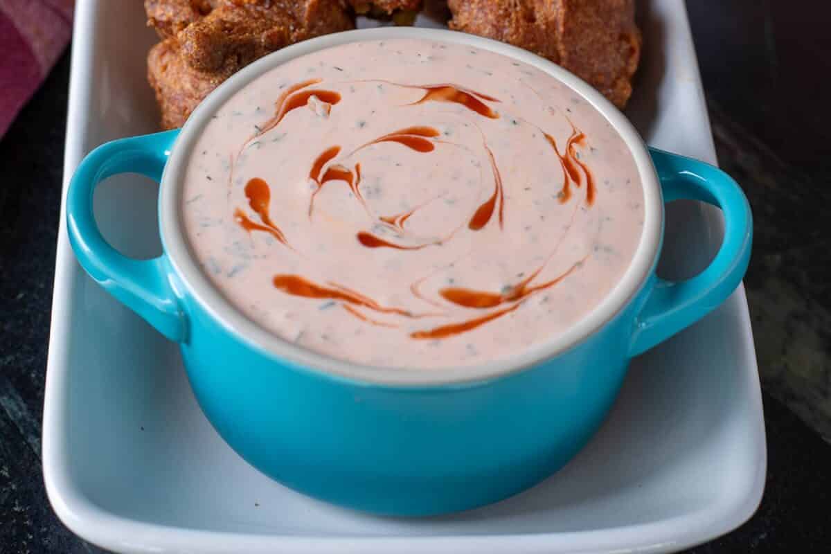 Buffalo ranch dip in a blue bowl on a white platter with hush puppies.