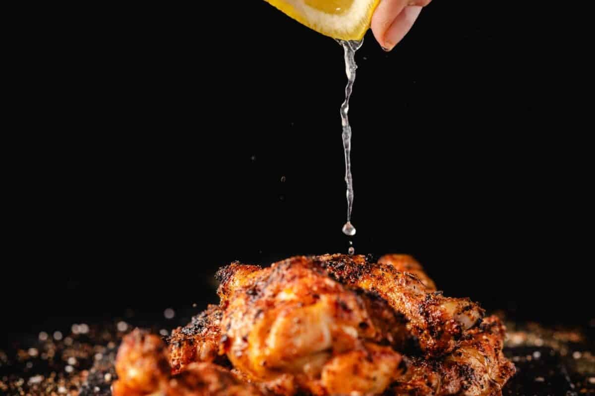 A lemon half being squeezed for juice over a chicken wing pile.