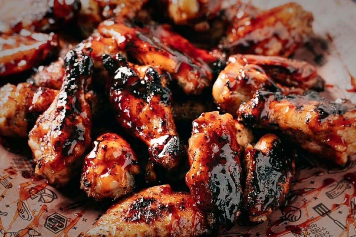 Honey BBQ wings stacked on a wooden cutting board.