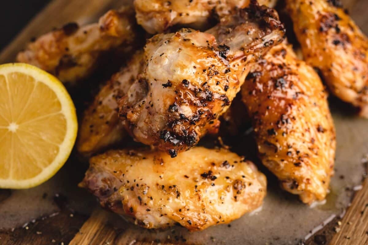 Lemon pepper chicken wings on a cutting board next to a lemon wedge.