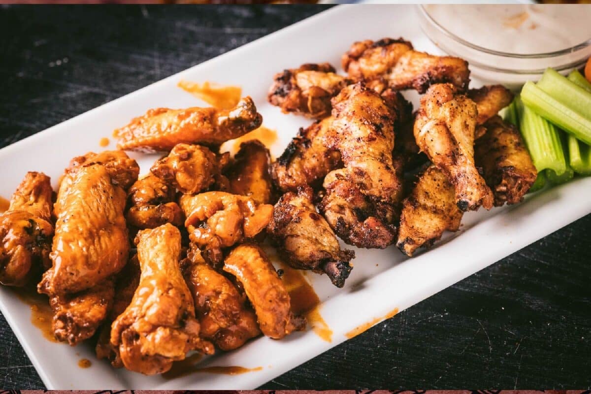 A white platter with chicken wings and a cup of sauce.