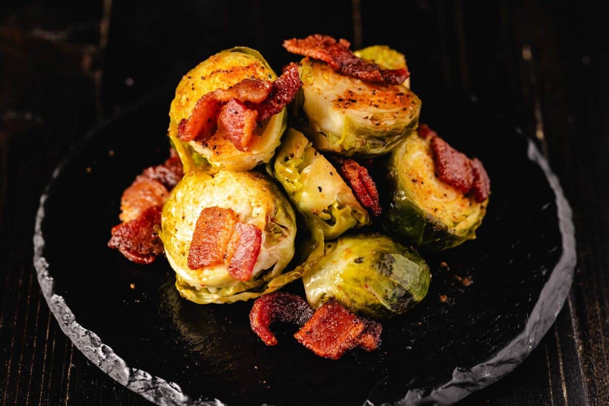 Grilled Brussels sprouts and bacon piled on a black serving platter.