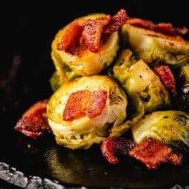 Grilled Brussels sprouts and bacon piled on a black serving platter.