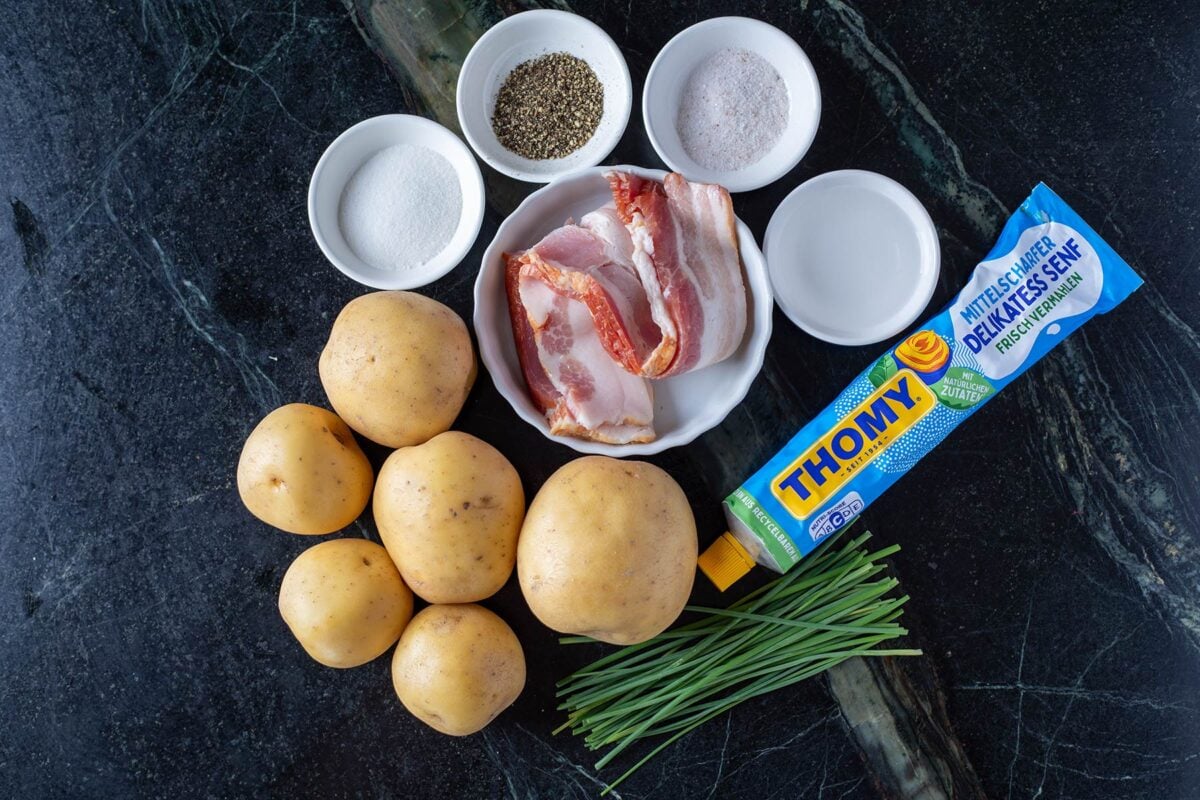 Potatos, chive, and Dijon mustard on a countertop with glass bowls on ingredients.