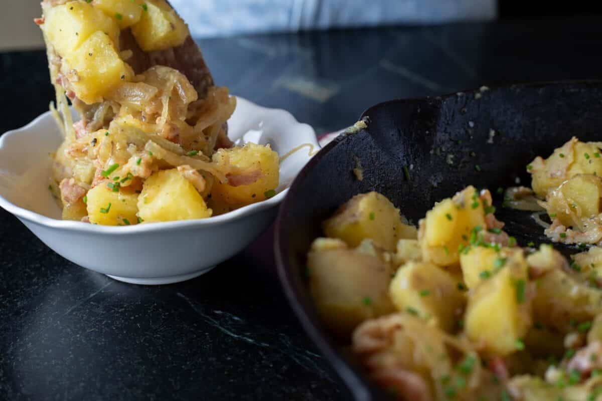 A white bowl and skillet, both full of German potato salad.