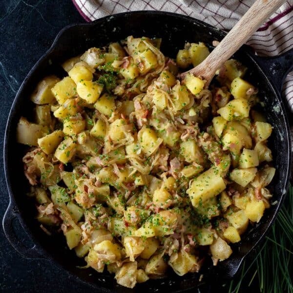 German potato salad in a cast iron skillet, with a wooden spoon resting in it.