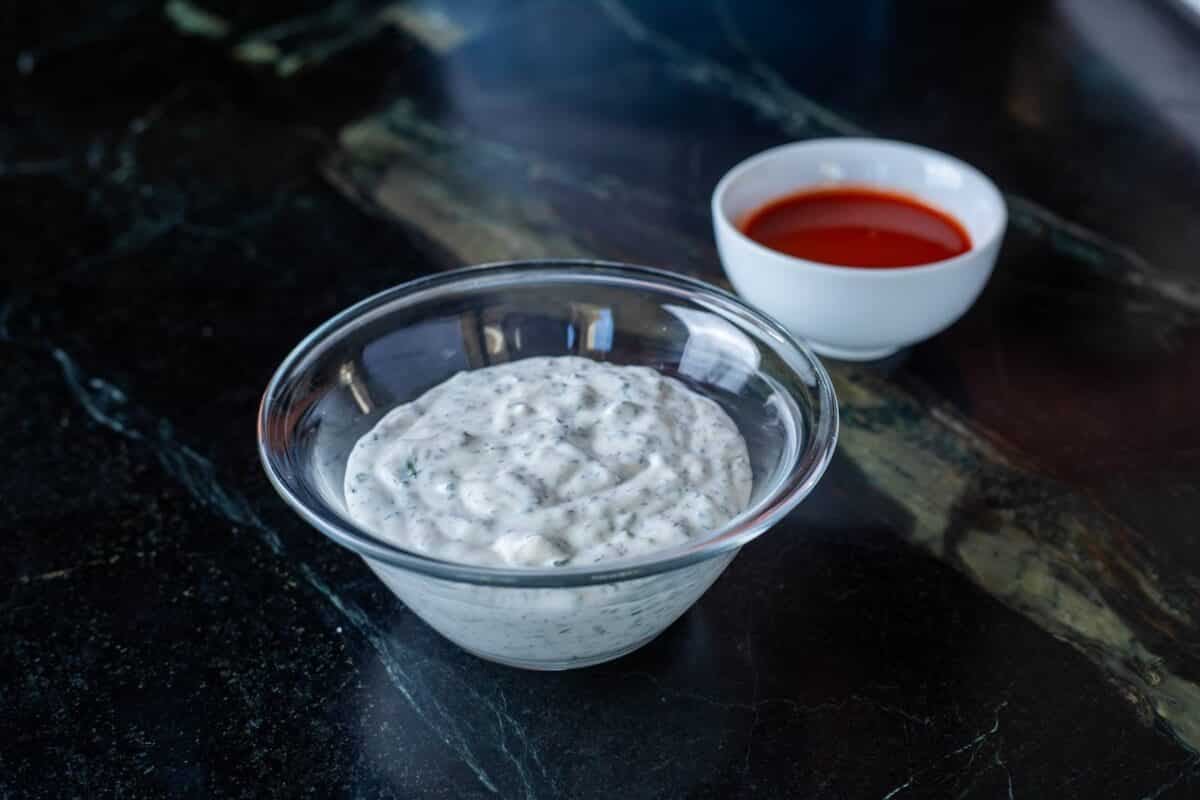 Bowls of ranch dressing and Buffalo sauce on a black countertop.