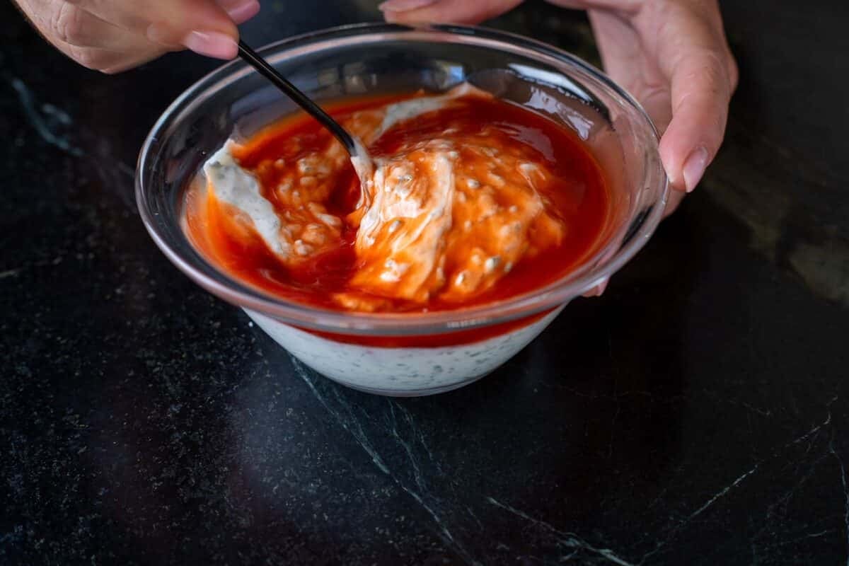 Hot sauce and dressing being mixed with a spoon in a glass bowl.