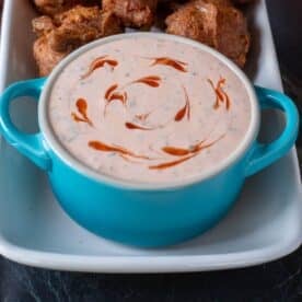 A blue bowl filled with Buffalo ranch dipping sauce, on a white plate with hush puppies.