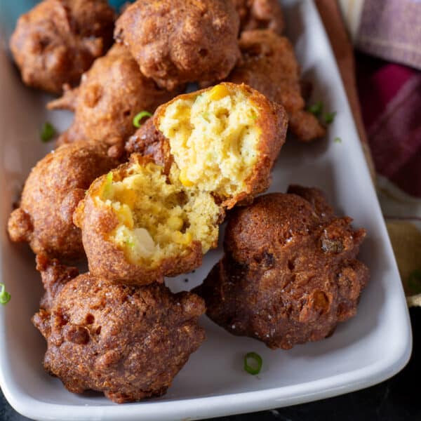 Hush puppies piled on a white plate, with the one on top broken in half.