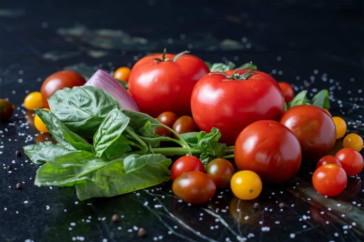 Fresh tomatoes, basil leaves, and onion grouped on a tabletop.