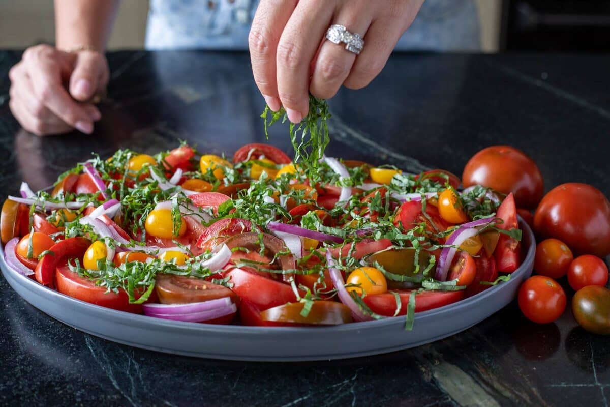 Fresh basil in slices being sprinkled onto a tomato salad on a serving platter.