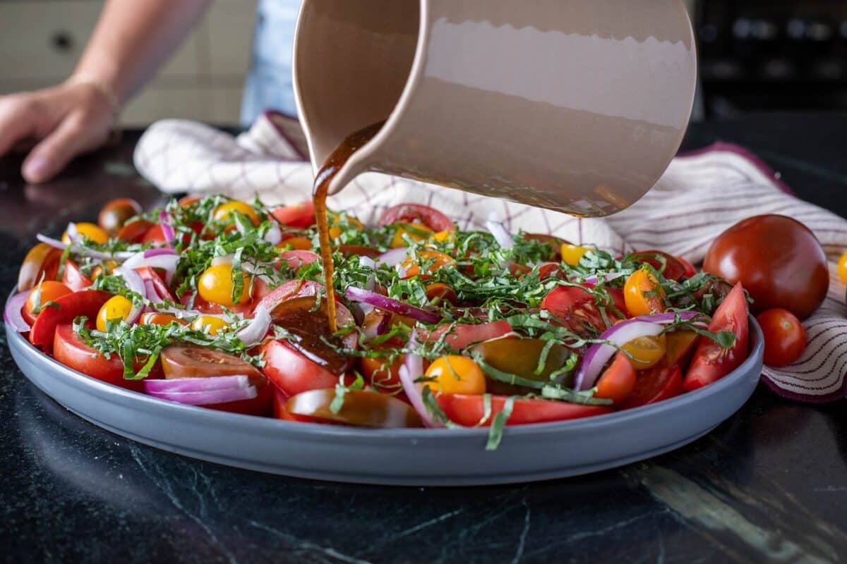 Salad on a platter being drizzled with dressing from a pitcher.